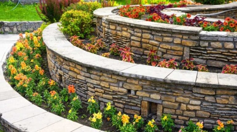 Landscaping with retaining walls and flowerbeds in residential house backyard. Landscape design of upscale home garden in summer. Flowers and plants on terraces in landscaped stone retaining walls.